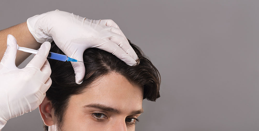 Mesotherapy of hair. Young man getting injections in head, grey panorama background, empty space