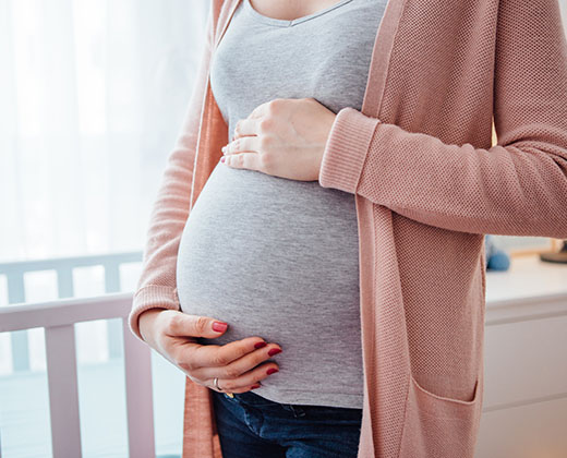 Pregnant young woman holding her belly. She is standing up next