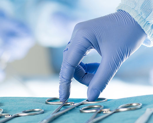 Close-up of scrub nurse taking medical instruments for operation with colleagues performing in background. Letter box format