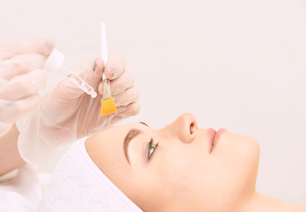 Young woman cleaning face skin in salon. Retinol peel with brush. Acid organic peeling.