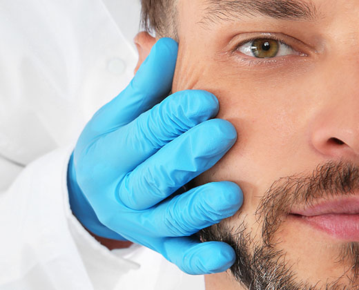 Doctor examining mature man face before cosmetic surgery on white background, closeup