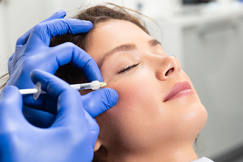 Attractive young woman is getting a rejuvenating facial injections. She is sitting calmly at clinic. The expert beautician is filling female wrinkles by hyaluronic acid.