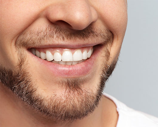 Everything should be perfect. Worried man with a stubble examining his nose and looking at camera while standing against grey background. Human face. Studio shot. Rhinoplasty